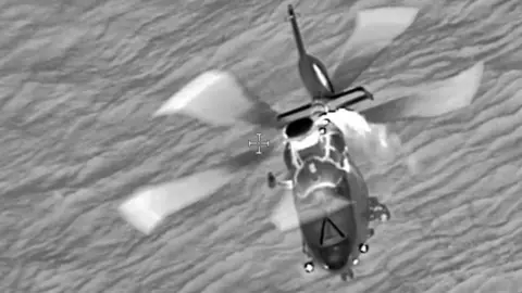 Channel Islands Air Search A black and white photo of a helicopter over the sea with rotors turning.