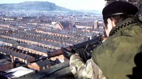 Getty Images A British soldier takes aim at a suspect from an observation post located on the roof of a tower block in the New Lodge, 20 February 1978