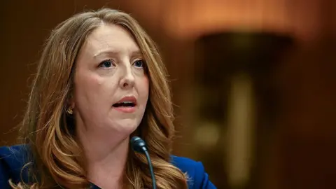 Means seen testifying to Congress, wearing a blue suit