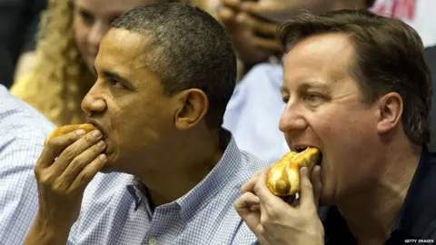 Getty Images Barack Obama and David Cameron eating hotdogs at a basketball game
