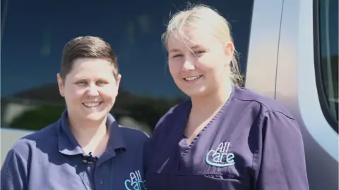 Rebecca and Jessica smiling at the camera in their carers uniform