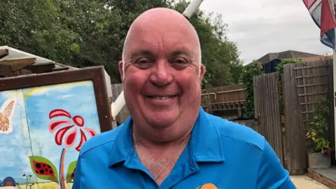 Kate Bradbrook/BBC Smiling man with very short hair wearing a blue shirt