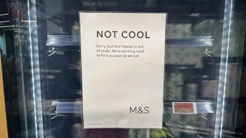 Jonny Mcguigan/BBC Supermarket freezer door, with sign saying: "NOT COOL Sorry, but this freezer is out of order. We're working hard to fix it as soon as we can."