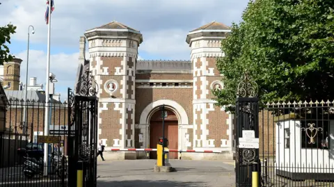 Wormwood Scrubs exterior - a red brick Victorian building with a traffic barrier outside 