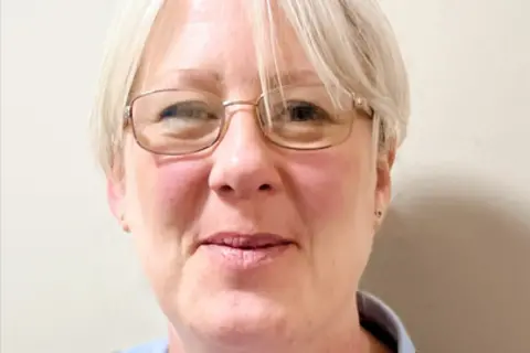 Nicola Rogers A woman with light coloured short hair and thin, metal framed glasses smiles into the camera.