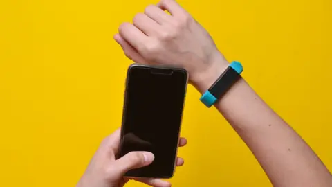 Getty Images Person holding a smartphone and wearing a linked device on their wrist