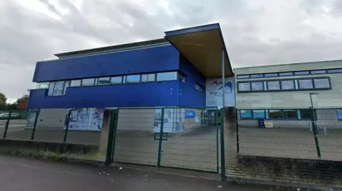 The exterior of the school, behind a tall green fence. 