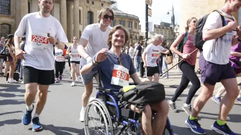 Tristan Boedts being pushed in a wheelchair by a friend in Broad Street in Oxford. 
