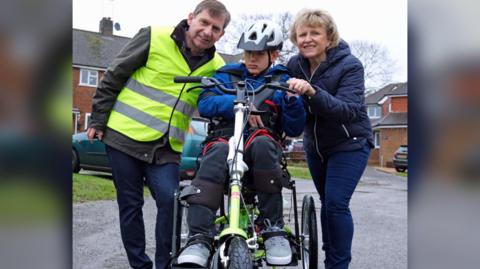 Mikey on a specially designed bike with his parents