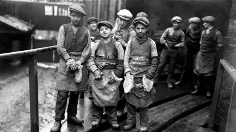 PA Media Group of children wearing aprons outside a factory in Swansea