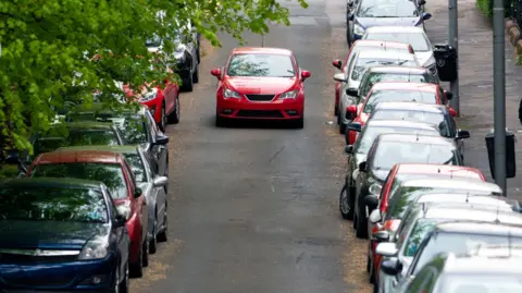 Car in the middle of a road with cars parked on either side in the UK - stock photo