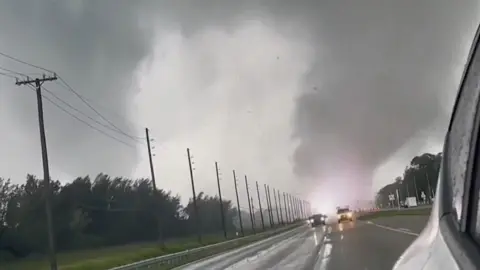 A representation   of a tornado astatine  the extremity  of a road, with cars connected  it, and a achromatic  flash wrong  it