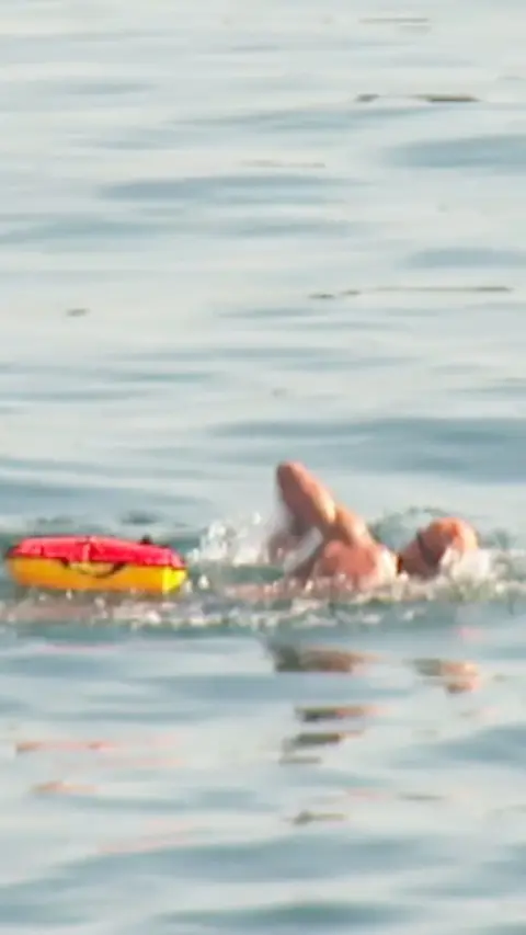 Man swimming in the sea with a red and yellow float beside him