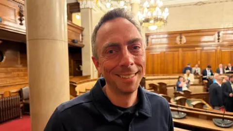 Becki Bowden / BBC A head and shoulder shot of councillor Mike Ross smiling at the camera. He has short grey hair and is wearing a black collared jumper. 