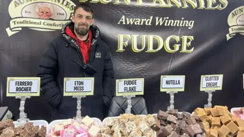 Rachel Russell/BBC Ashley, who was selling fudge on one of the stalls, stood behind the counter filled with different flavours of fudge