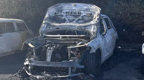 A close up of a burnt out car. The top is open.