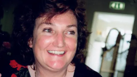 June Fox-Roberts smiling at a family gathering, with short brown curly hair and a black dress with red pattern on it