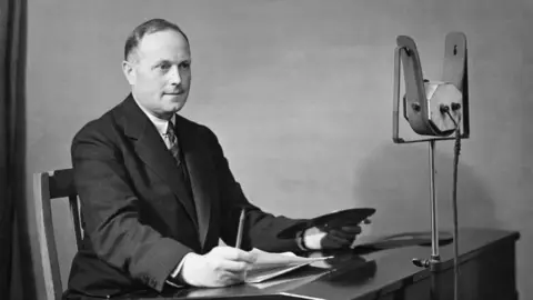 Arthur Burrows sits at a desk in front of a microphone