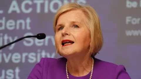 Donna Ockenden at the Nottingham maternity inquiry. She wears a purple dress and pearl necklace around her neck. She has blonde hair and is speaking into a microphone.