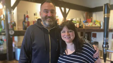 BBC/SimonThake James and Tasmin Kaminiski smile at the camera. James has short brown hair and a greying beard. He is wearing a navy hooded top. Tasmin has ling, dark hair and is wearing a blue and white striped top.