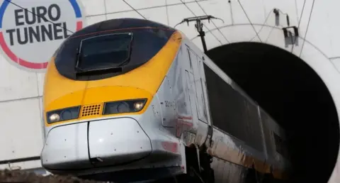 A yellow fronted train emerges from a tunnel with the words Euro Tunnel emblazoned in red, blue and black on the wall behind it