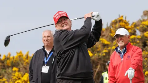 Dressed in a red hat, Donald Trump strikes a golf ball