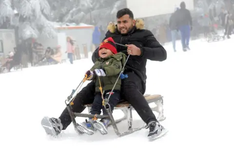 Getty Images A man and a boy ride a sledge in the snow.