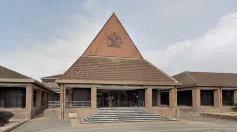 Google A Google Street image of the outside of Guildford Crown Court, which is a red bricked-building with a high roof. 