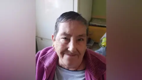 Supplied Family photograph of Sylvia Osler. She has short, dark hair and is wearing a pink cardigan. There is a fridge freezer in the background