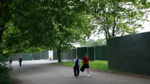 Reuters People walk on the road next to Heaton Park. Large black panels of fencing have been put up around the park.