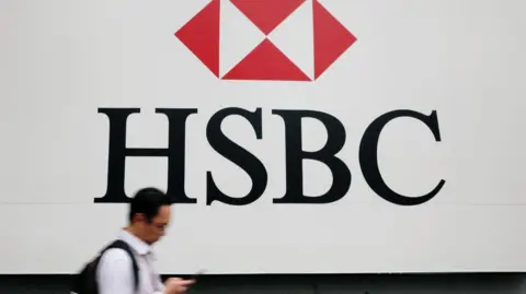 A man in a white shirt and black backpack walks past a large HSBC logo