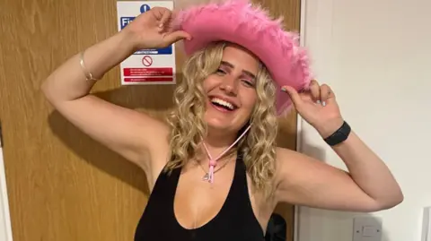 Phoebe Tesoriere wearing a pink cowboy hat, smiling at the camera. She is wearing a black top. She has blonde hair 