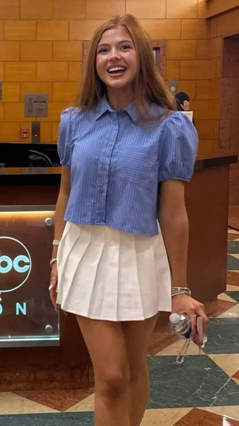 Sophie Lennon wearing a blue shirt and white skirt smiling at the camera 