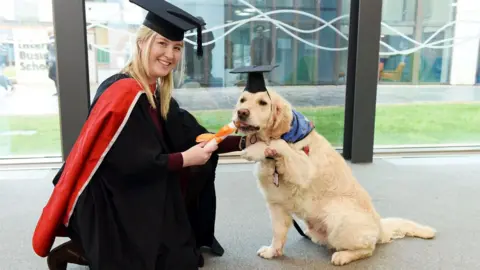Teesside University A woman in an academic gown presents a rolled up scroll