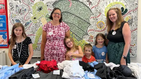 Bex and Faye stood with their young children. They are stood in front of a table of folded clothes