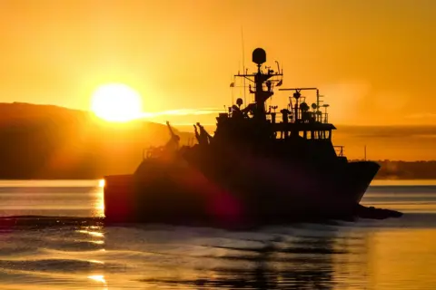 Tommy Bamford  Fishery patrol vessel Minna returning on the River Clyde, with bright sun in the background

