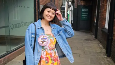 Nina Nina, a young woman who smiles in the camera. He wears a floral color with a denim jacket on it.