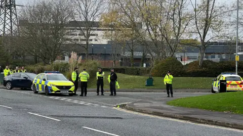 Two market police cars and several police parked at the corner of a road.