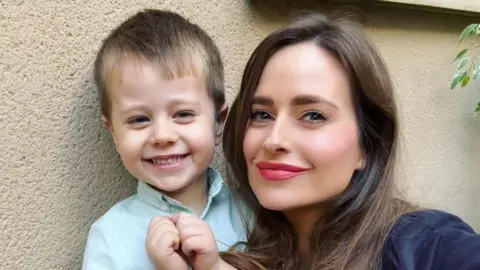 A woman crouched next to a child. They are both smiling.