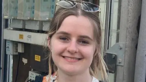 Family handout A head and shoulders picture of a young blonde girl wearing sunglasses and smiling at the camera.