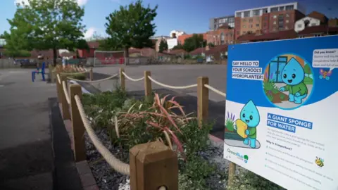 Two fences off garden areas in a playground with a blue and white sign and text which says "Say hello to your school's hydroplanter". "A giant sponge for water".