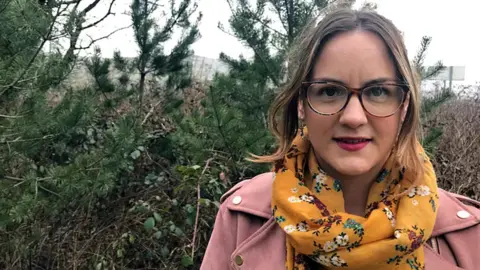 BBC Kirsty James wearing a pink coat and yellow floral scarf and glasses