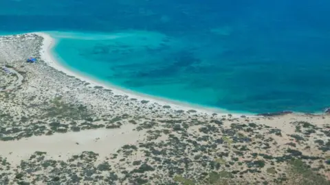 Getty Images Uma costa árida vista do ar, com águas do mar turquesa e manchas escuras de recife