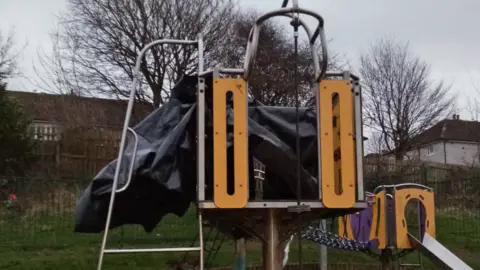 Workington Town Council A piece of grey and yellow play park equipment is covered in a black piece of plastic.