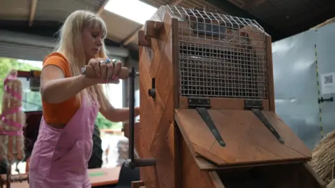Shaun Whitmore/BBC A woman makes use of a wooden piece of equipment during the processing of a crop to turn it into fabric. 
