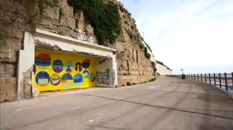 Steve Morgan A concrete structure is built into a cliff on a coastal promenade.