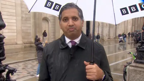 Faisal Islam holding a white BBC umbrella