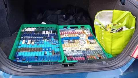 The open boot of a blue car showing hundreds of packets of cigarettes and tobacco.