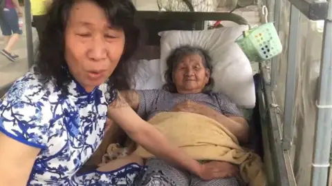 Pear video Still from the video showing the man with his mother while dressed in a traditional Chinese dress and with long hair