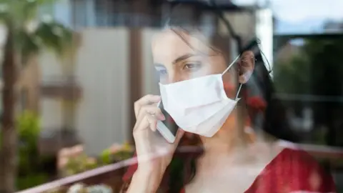 Getty Images Woman wearing face mask looking out of window